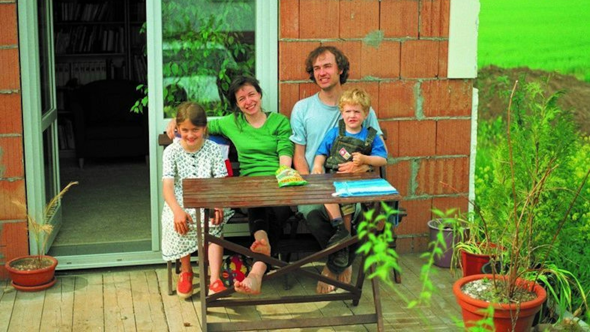 Eine Familie mit zwei Kindern sitzt lachend auf der Gartenterrasse.