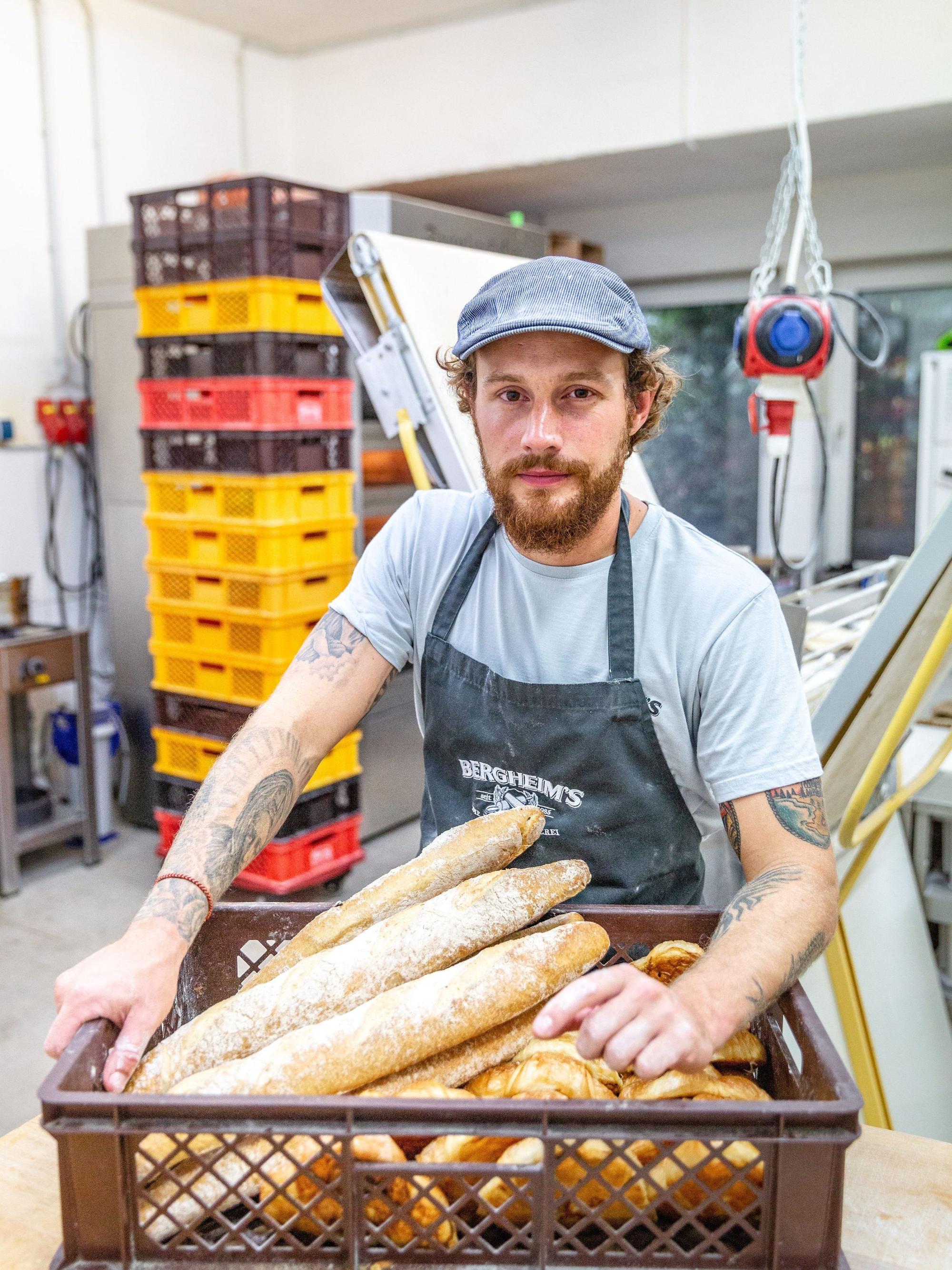 Bäckermeister Tim Bergheim steht mit einem Korb voller Ciabatta-Brote in der Backstube der Bäckerei "Bergheim's - Die Meisterbäckerei".