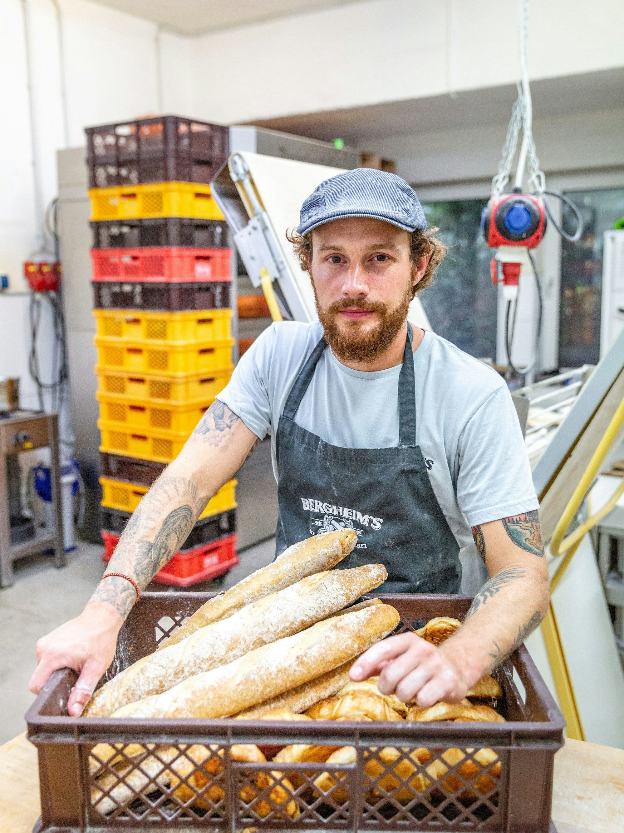 Bäckermeister Tim Bergheim steht mit einem Korb voller Ciabatta-Brote in der Backstube der Bäckerei "Bergheim's - Die Meisterbäckerei".