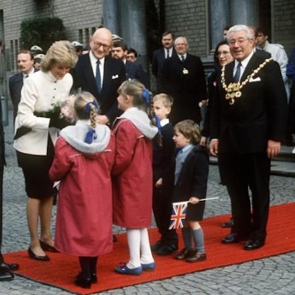 Der britische Kronprinz Charles (l) und seine Gattin Prinzessin Diana am 03.11.1987 in Köln. Während der Kronprinz sich umschaut und nach oben blickt, überreichen Kinder seiner Ehefrau Blumen. Rechts im Bild: Norbert Burger, damaliger Oberbürgermeister von Köln.