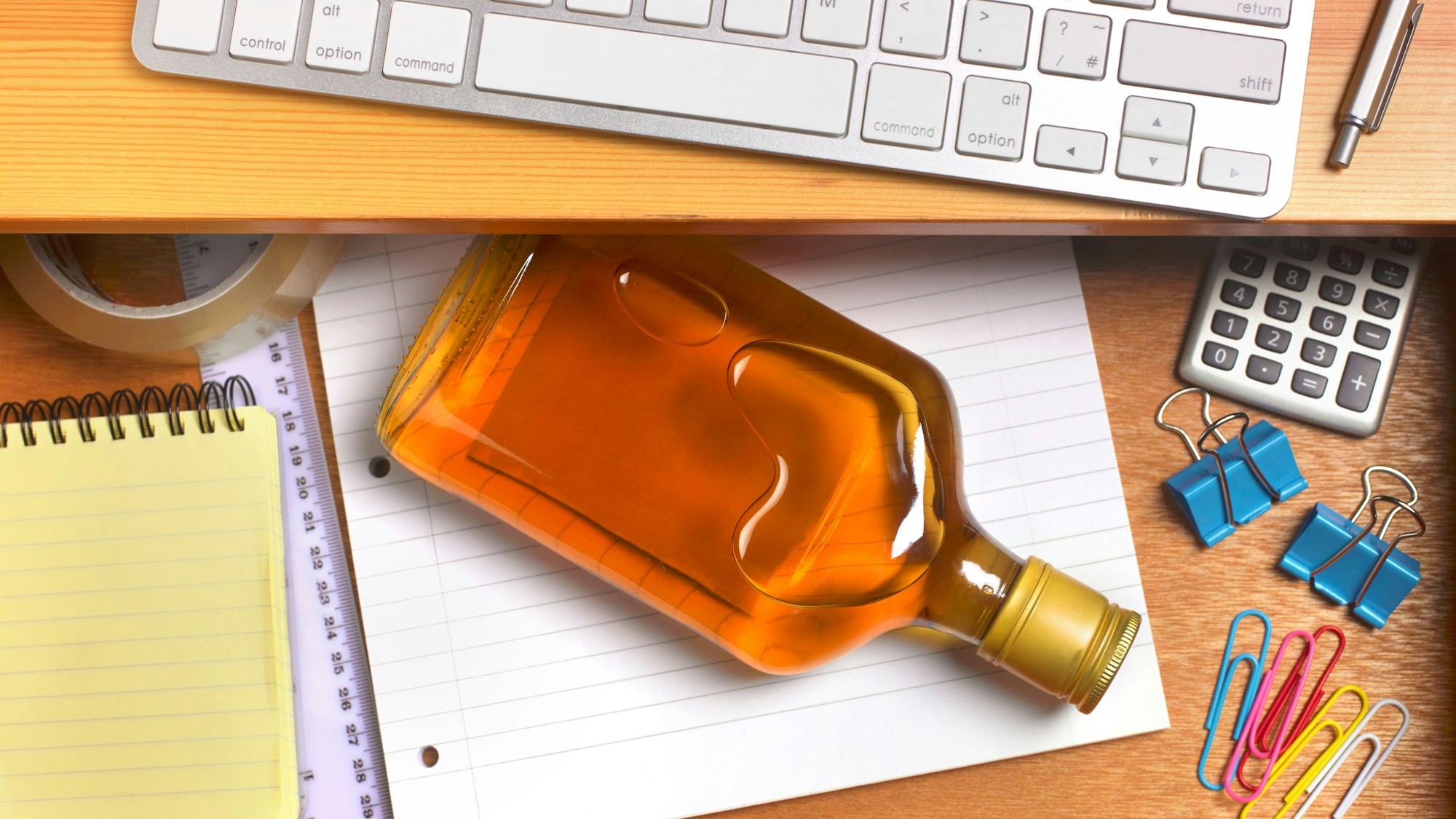 Eine Schnapsflasche liegt in einer Schreibtischschublade zwischen Büroutensilien.