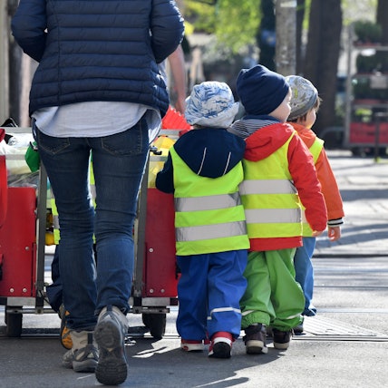 Eine Tagesmutter läuft mit mehreren Kleinkindern über eine Straße.