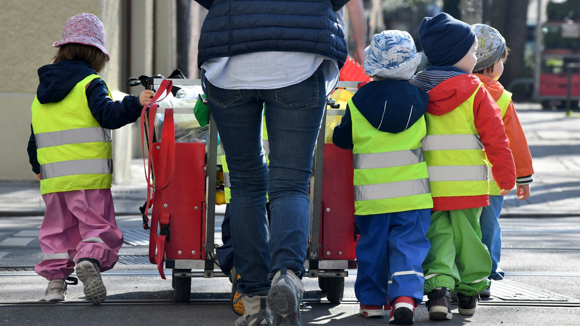 Eine Erzieherin läuft mit mehreren Kleinkindern über einen Bürgersteig