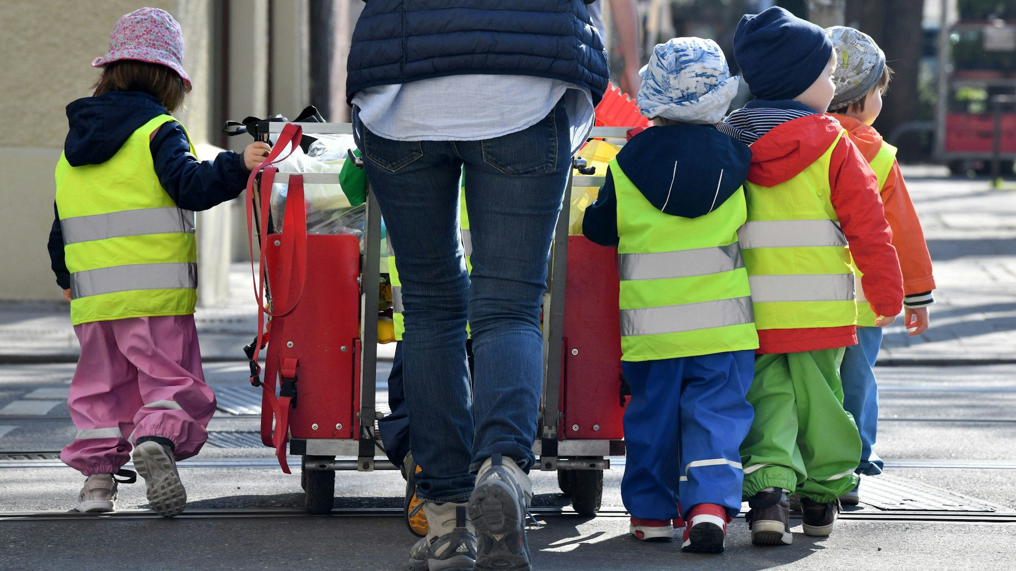 Eine Tagesmutter läuft mit mehreren Kleinkindern über eine Straße.