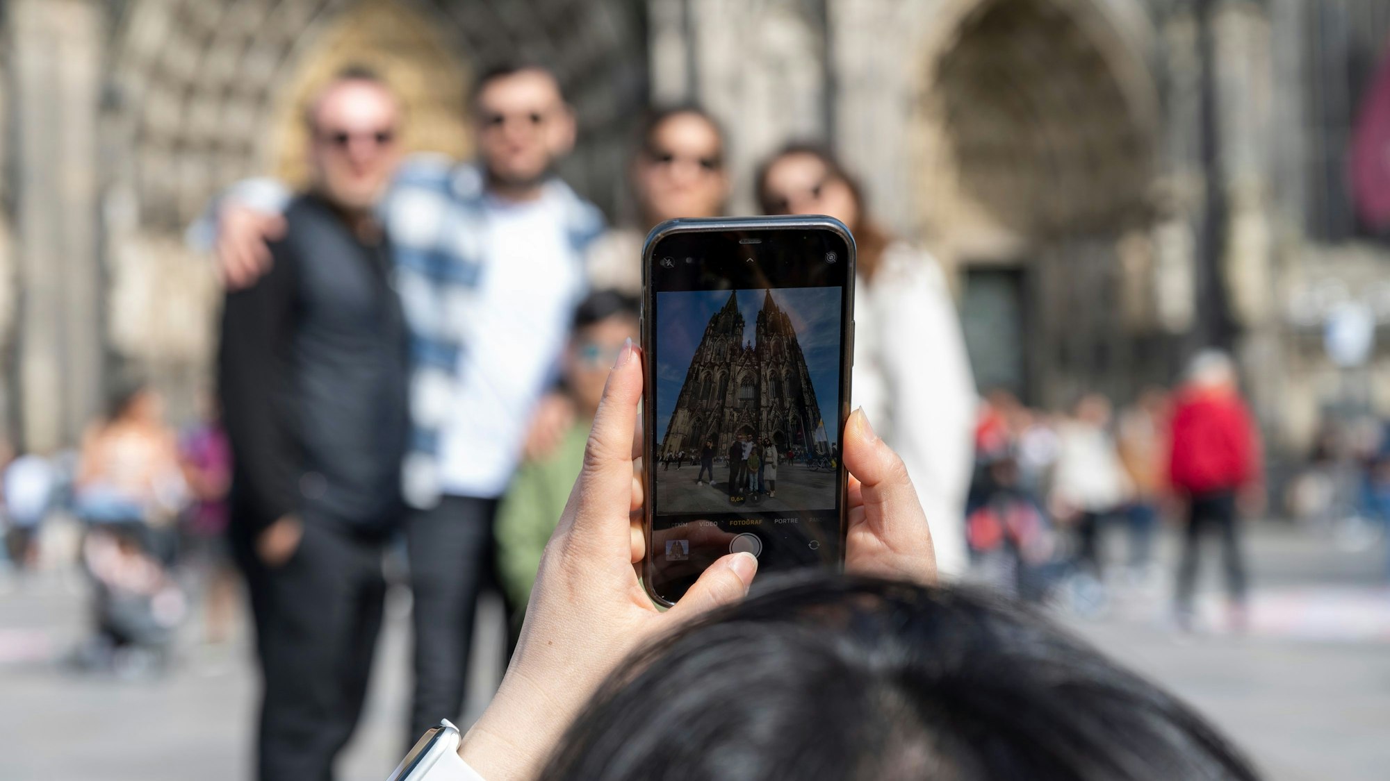 Eine Frau fotografiert Touristen vor dem Dom.