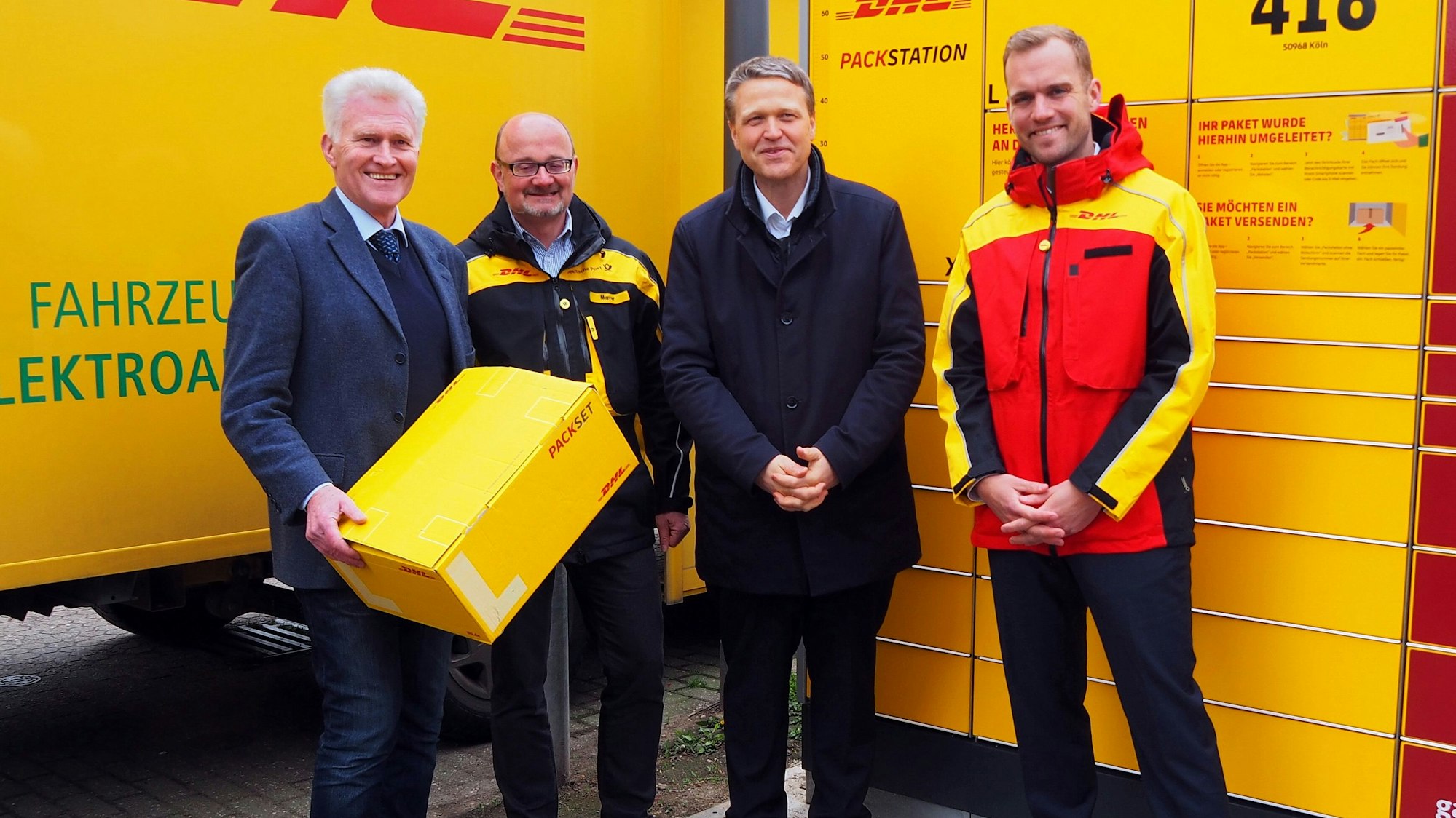 Vier Männer stehen vor einem DHL-Lieferwagen und der neuen Packstation.