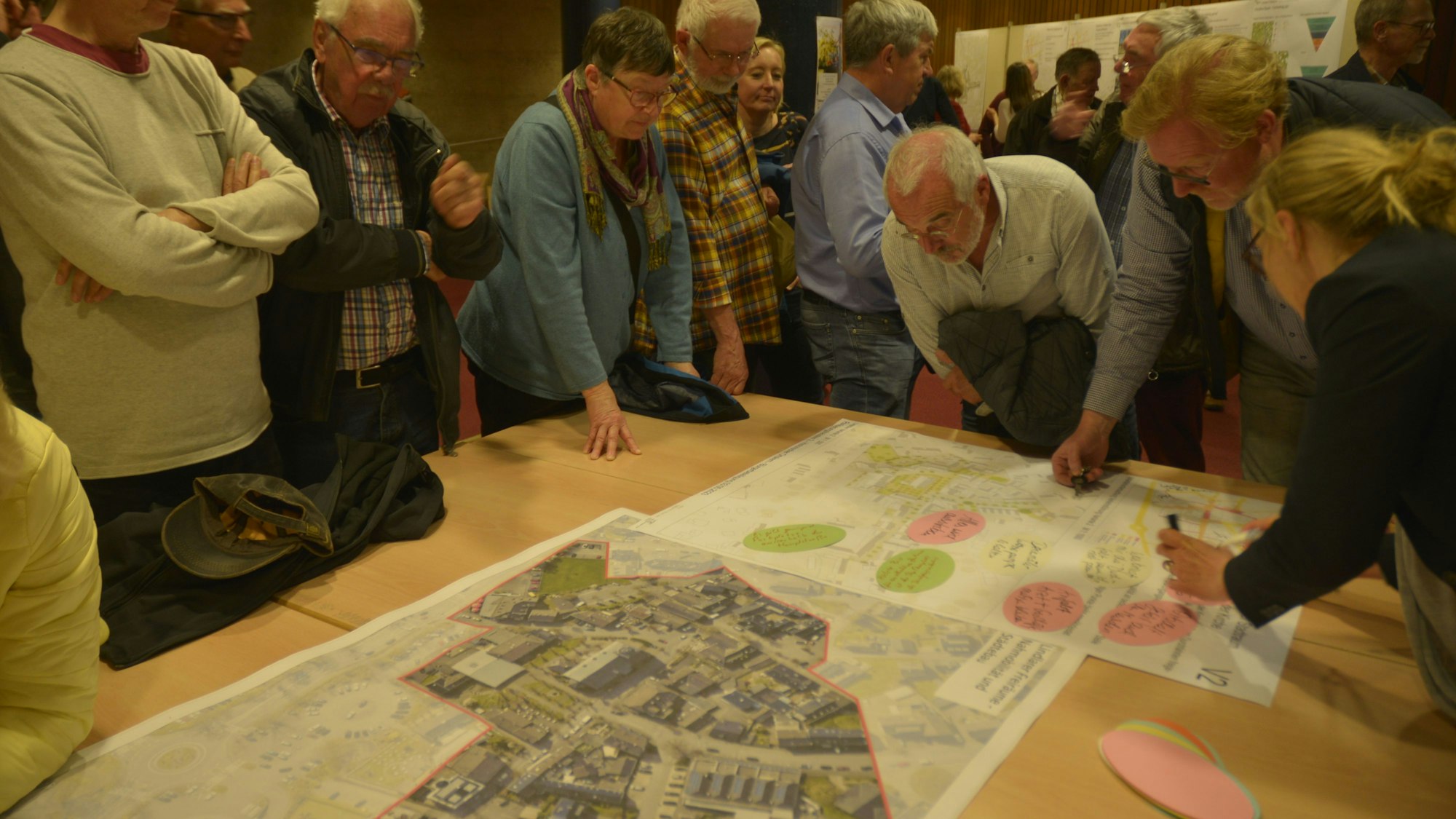 Bürgerinnen und Bürger stehen um einen Tisch versammelt. Auf dem Tisch ausgebreitet liegen Karten mit den Planungen.