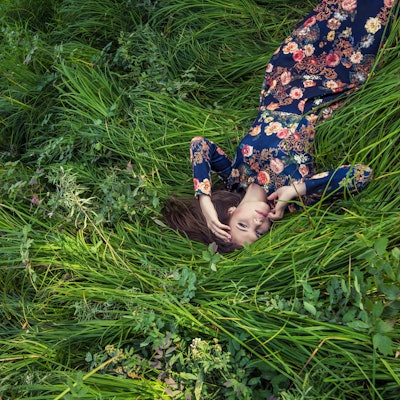 Eine Frau in einem geblümten Kleid liegt mitten in einer sehr grünen Wiese.