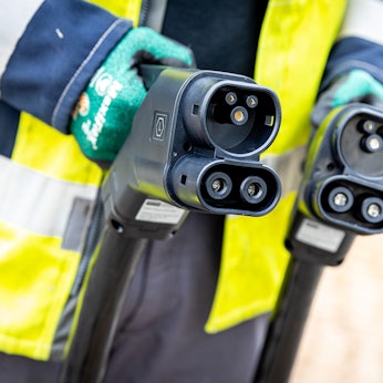 Ein Techniker hält nach der Installation einer Ladesäule für Elektroautos zwei Ladekabel in seinen Händen.