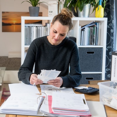 Frau am Schreibtisch mit Aktenordner sortiert Quittungen.