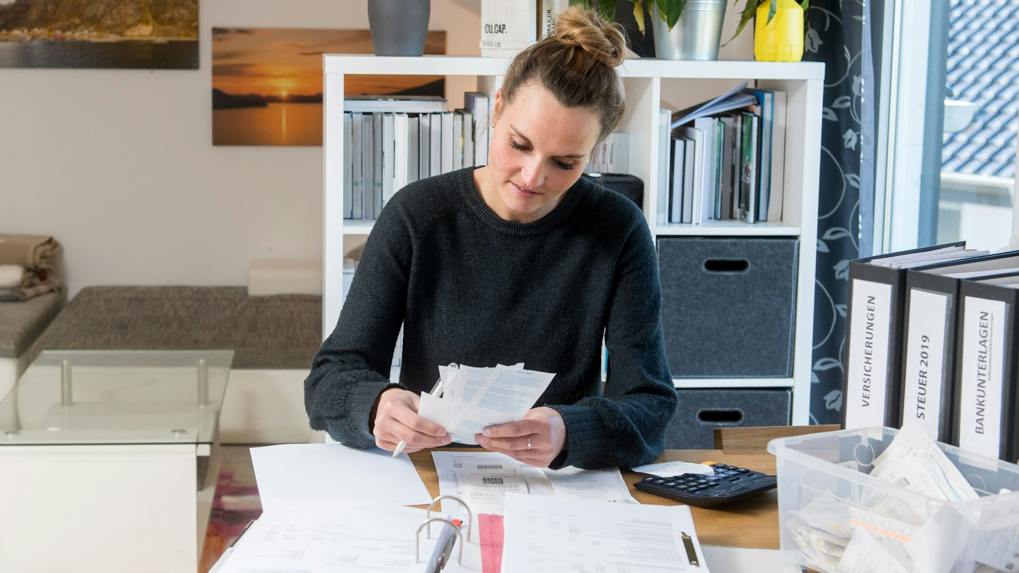 Frau am Schreibtisch mit Aktenordner sortiert Quittungen.