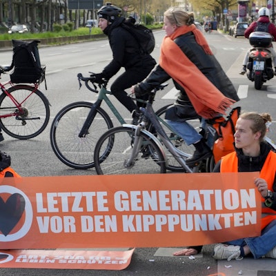 Cyclists drive unhindered past climate activists who have their hands glued to the ground during a climate protest in Berlin, Germany, Thursday, April 27, 2023. Activists of the 'Letzte Generation' (Last Generation) blocked streets in Berlin on Thursday to protest against the climate policy of the German government. (AP Photo/Michael Sohn)