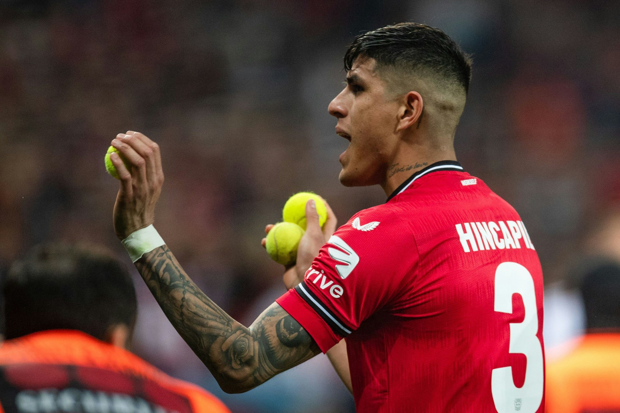 Leverkusens Piero Hincapie sammelt Tennisbälle auf, die Kölner Fans auf den Rasen geworfen haben.