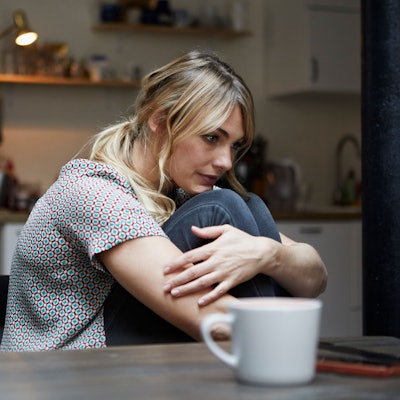 Eine Frau sitzt etwas zusammengekauert alleine an einem Tisch und starrt ins Leere