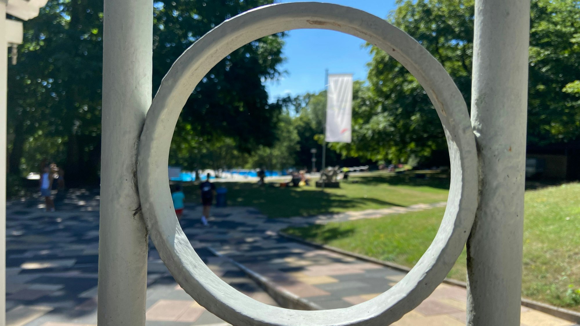 Auf dem Bild ist der Eingangszaun des Freibades und ein Blick auf die Liegewiesen zu sehen.