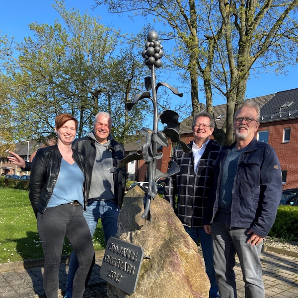 Die Mitglieder des Kultur- und Heimtvereins Grefrath lachen in die Kamera und stehen vor einem Denkmal.