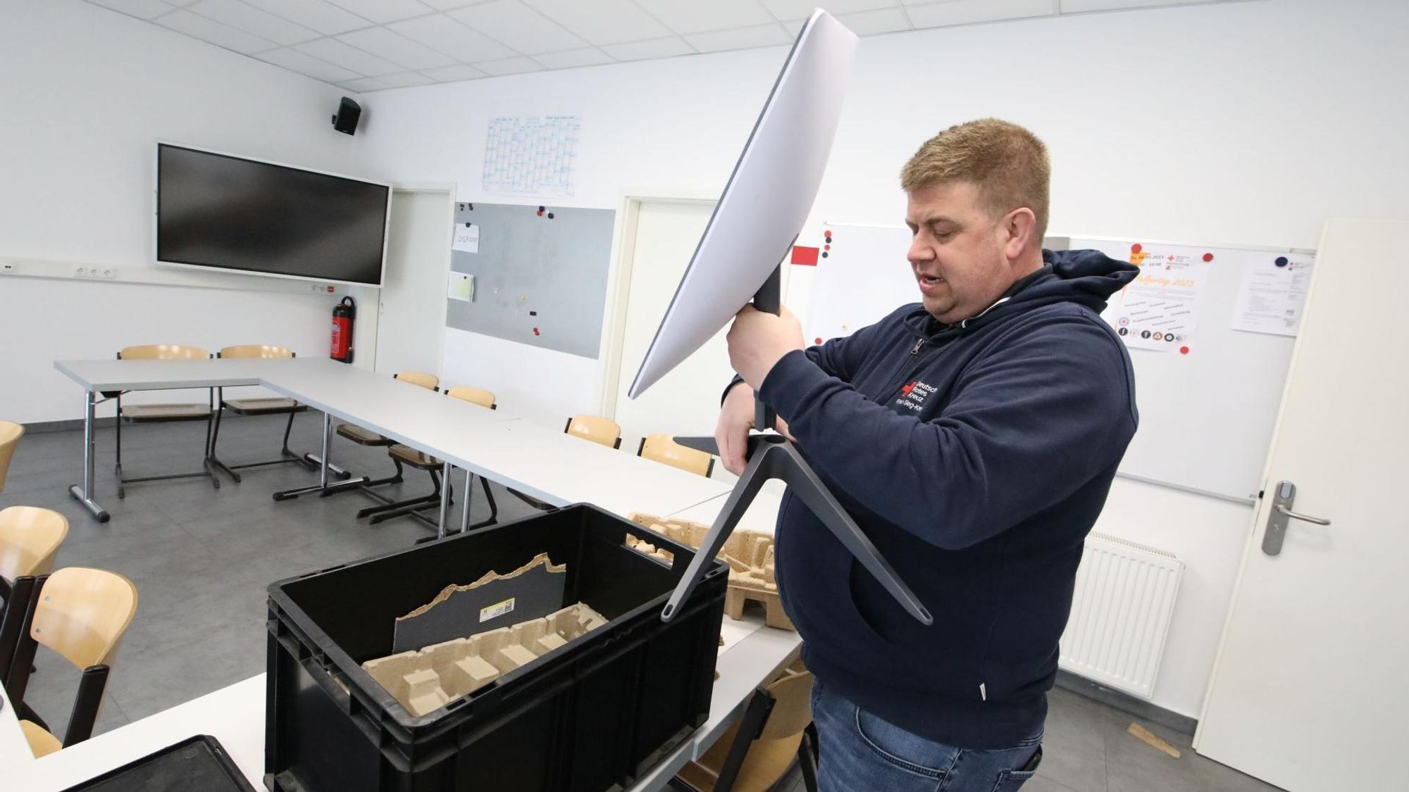 Ein Mann hält eine weiße Satellitenschüssel in der Hand und montiert sie an einen Ständer. Auf dem Tisch davor steht eine schwarze Kiste.