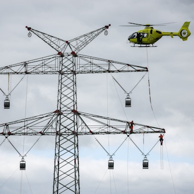 Schleswig-Holstein, Klixbüll: Ein Hubschrauber fliegt beim Einziehen der sogenannten Vorseile zwischen den Strommasten des letzten Bauabschnitts der Westküstenleitung. Mit dem Hubschrauber werden leichte Kunststoffseile von Mast zu Mast geflogen, Industriemonteure führen das Vorseil durch Rollen an den Mastenden. Die Westküstenleitung - eine 380-Kilovolt-Freileitung - wird über insgesamt rund 140 Kilometer zwischen Brunsbüttel und der dänischen Grenze und von dort weiter verlaufen.