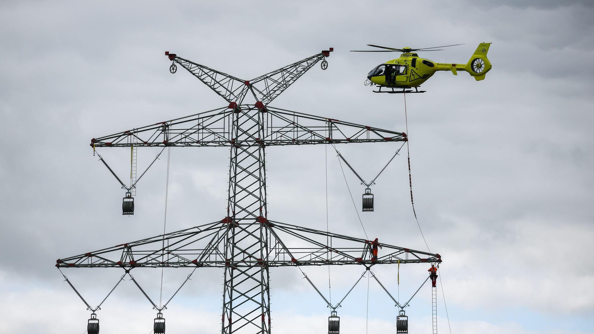 Schleswig-Holstein, Klixbüll: Ein Hubschrauber fliegt beim Einziehen der sogenannten Vorseile zwischen den Strommasten des letzten Bauabschnitts der Westküstenleitung. Mit dem Hubschrauber werden leichte Kunststoffseile von Mast zu Mast geflogen, Industriemonteure führen das Vorseil durch Rollen an den Mastenden. Die Westküstenleitung - eine 380-Kilovolt-Freileitung - wird über insgesamt rund 140 Kilometer zwischen Brunsbüttel und der dänischen Grenze und von dort weiter verlaufen.