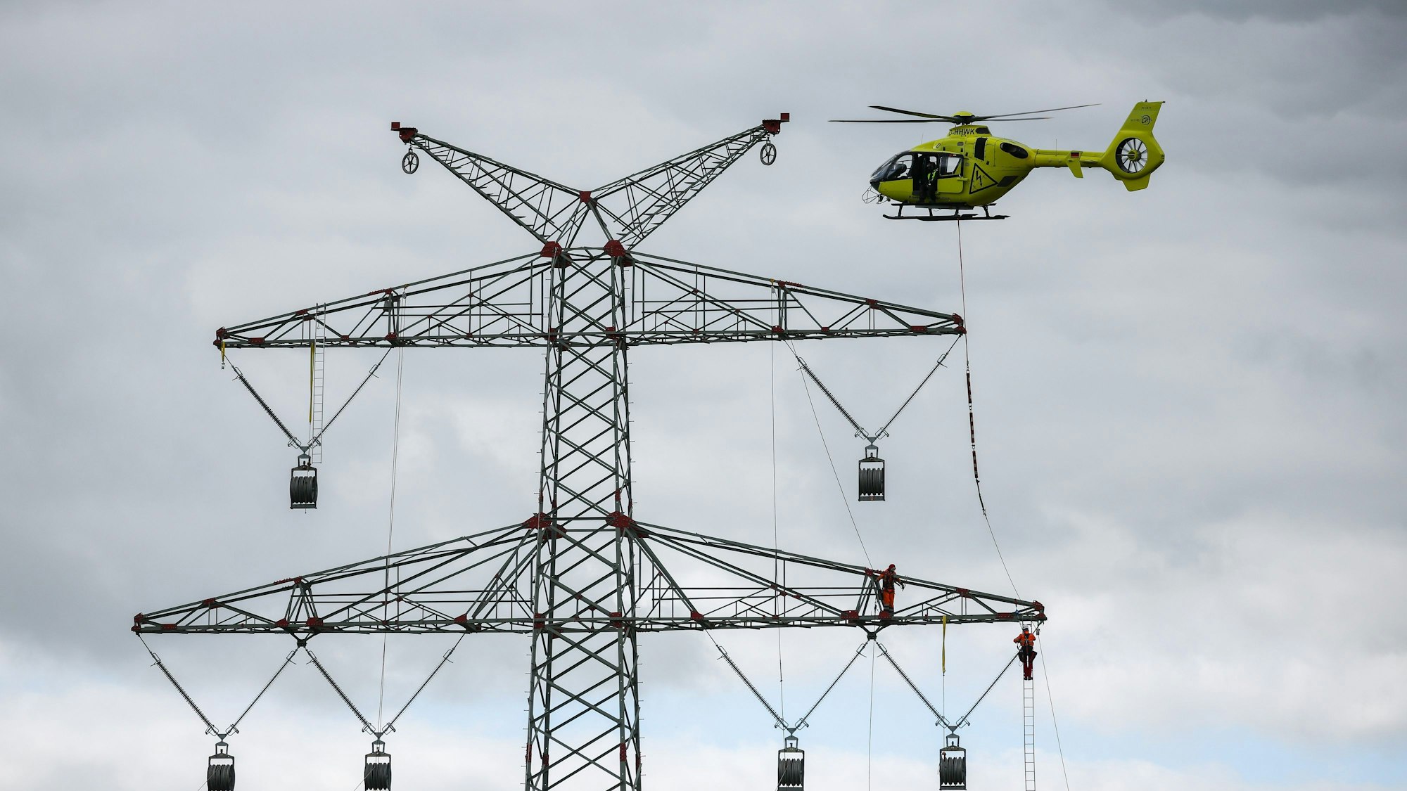 Schleswig-Holstein, Klixbüll: Ein Hubschrauber fliegt beim Einziehen der sogenannten Vorseile zwischen den Strommasten des letzten Bauabschnitts der Westküstenleitung. Mit dem Hubschrauber werden leichte Kunststoffseile von Mast zu Mast geflogen, Industriemonteure führen das Vorseil durch Rollen an den Mastenden. Die Westküstenleitung - eine 380-Kilovolt-Freileitung - wird über insgesamt rund 140 Kilometer zwischen Brunsbüttel und der dänischen Grenze und von dort weiter verlaufen.
