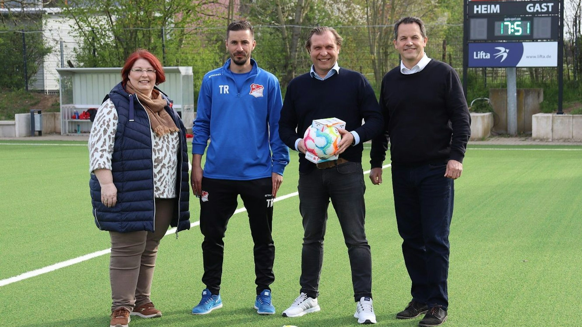 Ortsvorsteherin Birgitt Baus, Jugendleiter Dennis Frère, Patrick Gartmann, Vorsitzender des SC Germania 1932 Geyen und Bürgermeister Frank Keppeler stehen auf dem Kunstrasenplatz.