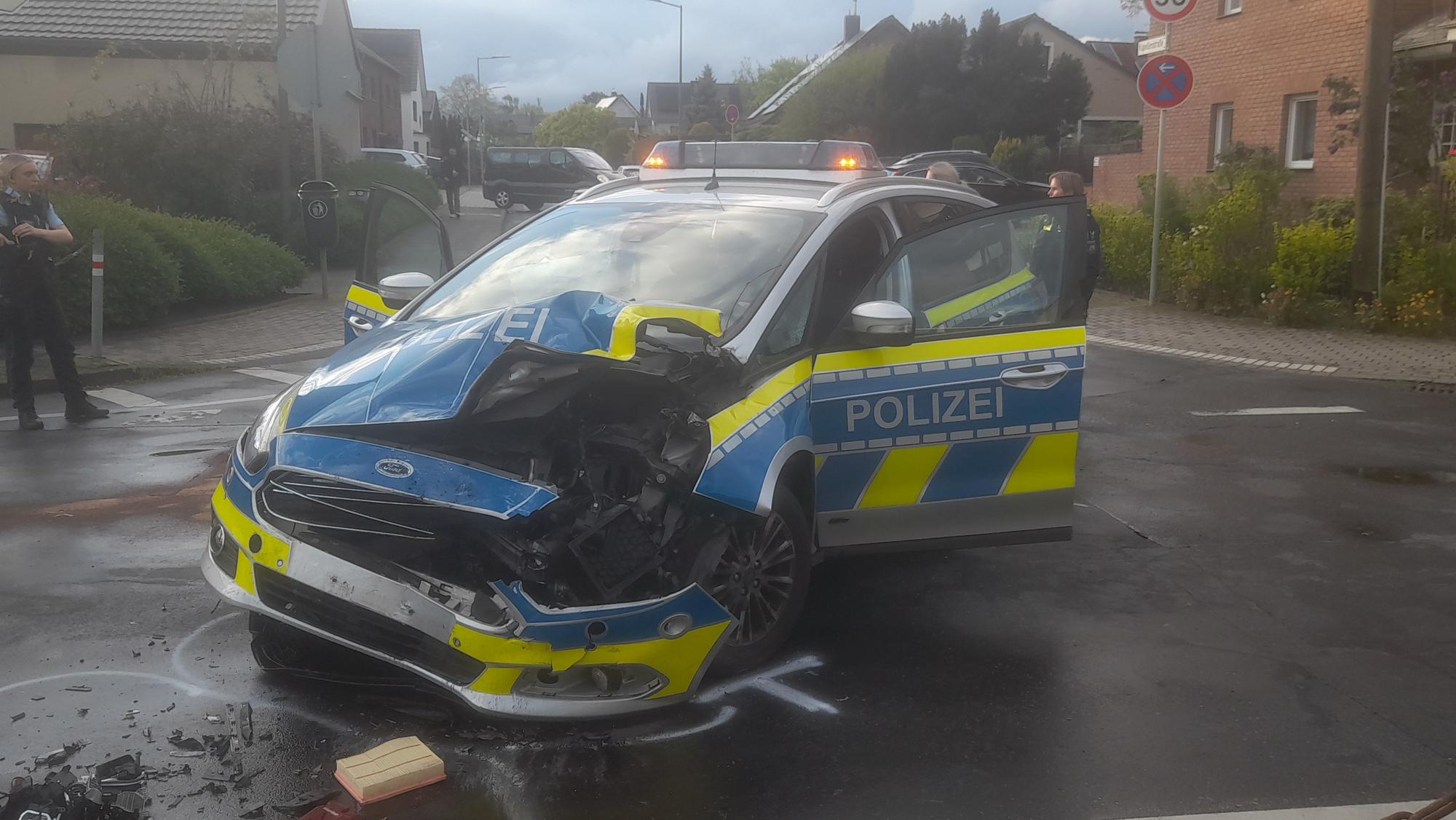 Ein Polizeiauto steht schwer beschädigt auf einer Kreuzung. Die linke Fron des Wagens ist aufgerissen und zerbeult.
