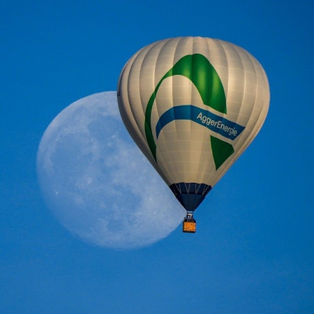 Ein Heißluftballon mit dem Logo der Aggerenergie fliegt am Himmel. Im Hintergrund des Ballons ist groß der Mond zu sehen.