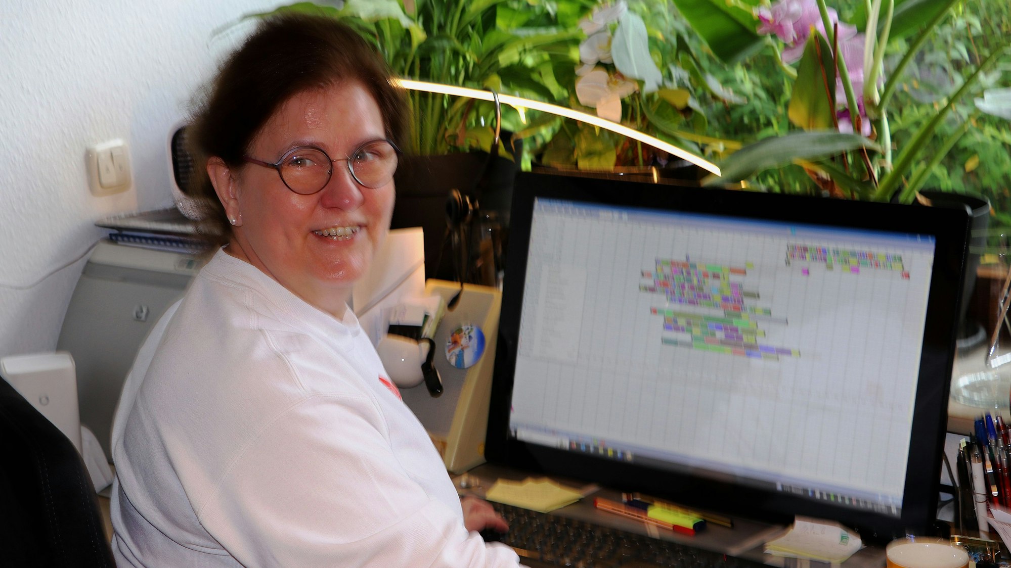 Inge Hartmann sitzt am PC, ein Schichtplan ist geöffnet. Sie lächelt in die Kamera.