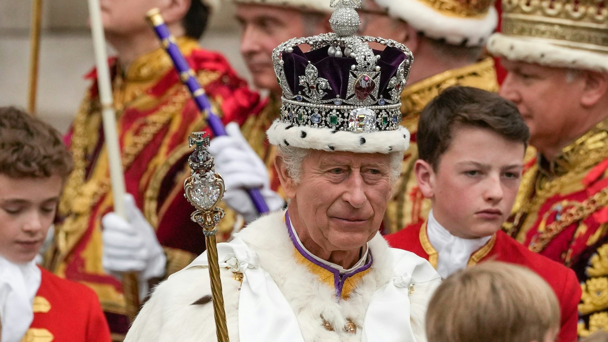 König Charles III. verlässt nach der Krönungszeremonie mit der Imperial State Crown, einem Zepter und dem Reichsapfel die Westminster Abbey.