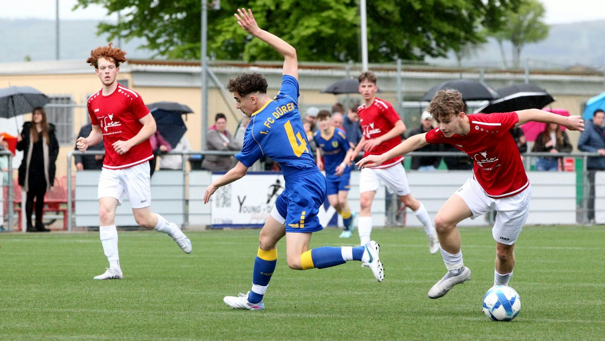 Ein Spieler der JSG Erft 01 im roten Trikot und weißer Hose lässt einen Spieler des 1. FC Düren II ganz in blau aussteigen.