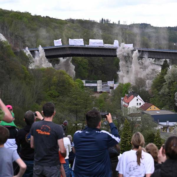 People take pictures of the Rahmede highway bridge during its blasting on May 7, 2023 on the A45 motorway, near Luedenscheid, western Germany. - During a routine inspection of the 453-metre-long Rahmede viaduct in December 2021, inspectors discovered deformations in the steel wall that could affect the bridge's load-bearing capacity. According to the motorway company, a new construction will take at least five years. (Photo by INA FASSBENDER / AFP)