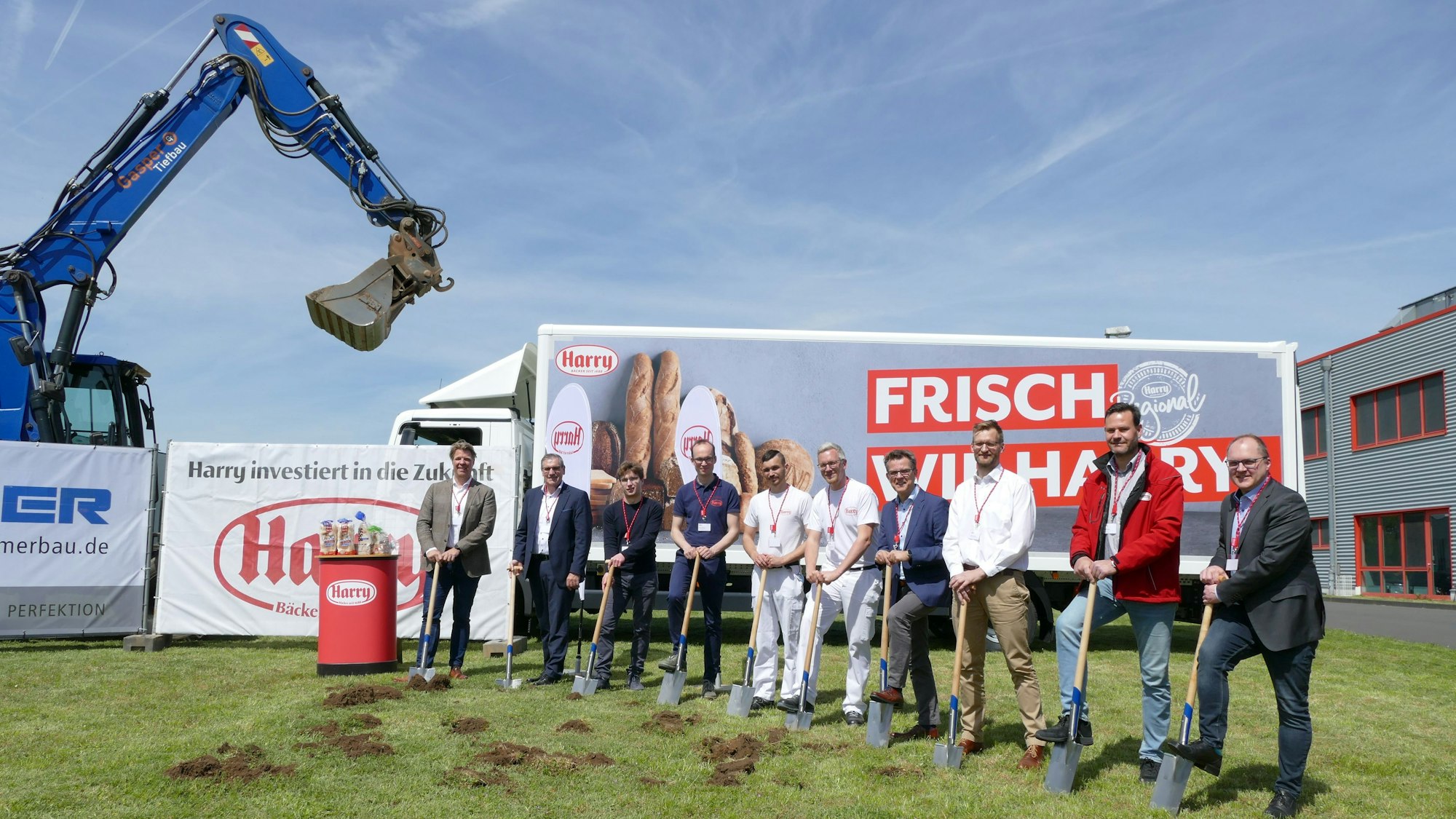 Wichtige Menschen von Harry Brot beim Spatenstich, im Hintergrund sieht man einen Bagger und einen LKW mit dem Firmen-Logo.