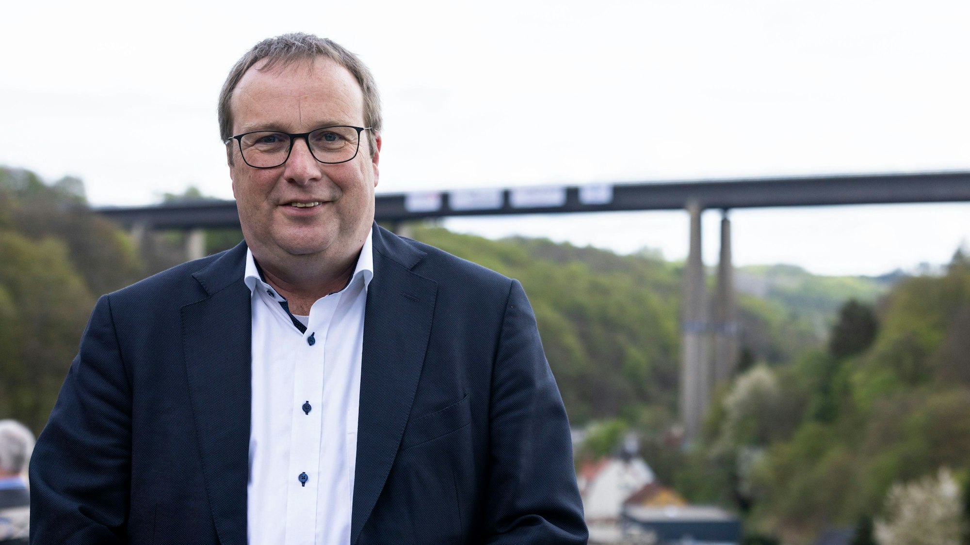 Oliver Krischer (Bündnis 90/Die Grünen), Minister für Umwelt, Naturschutz und Verkehr des Landes Nordrhein-Westfalen, schaut sich die Sprengung der Rahmede-Talbrücke vor Ort an. Krischer blickt in die Kamera, hinter ihm in einiger Entfernung ist die Talbrücke zu sehen.