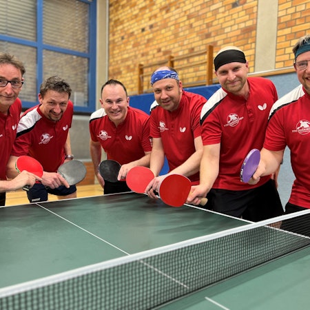 Sechs Tischtennisspieler posieren mit Schläger an einer Platte.