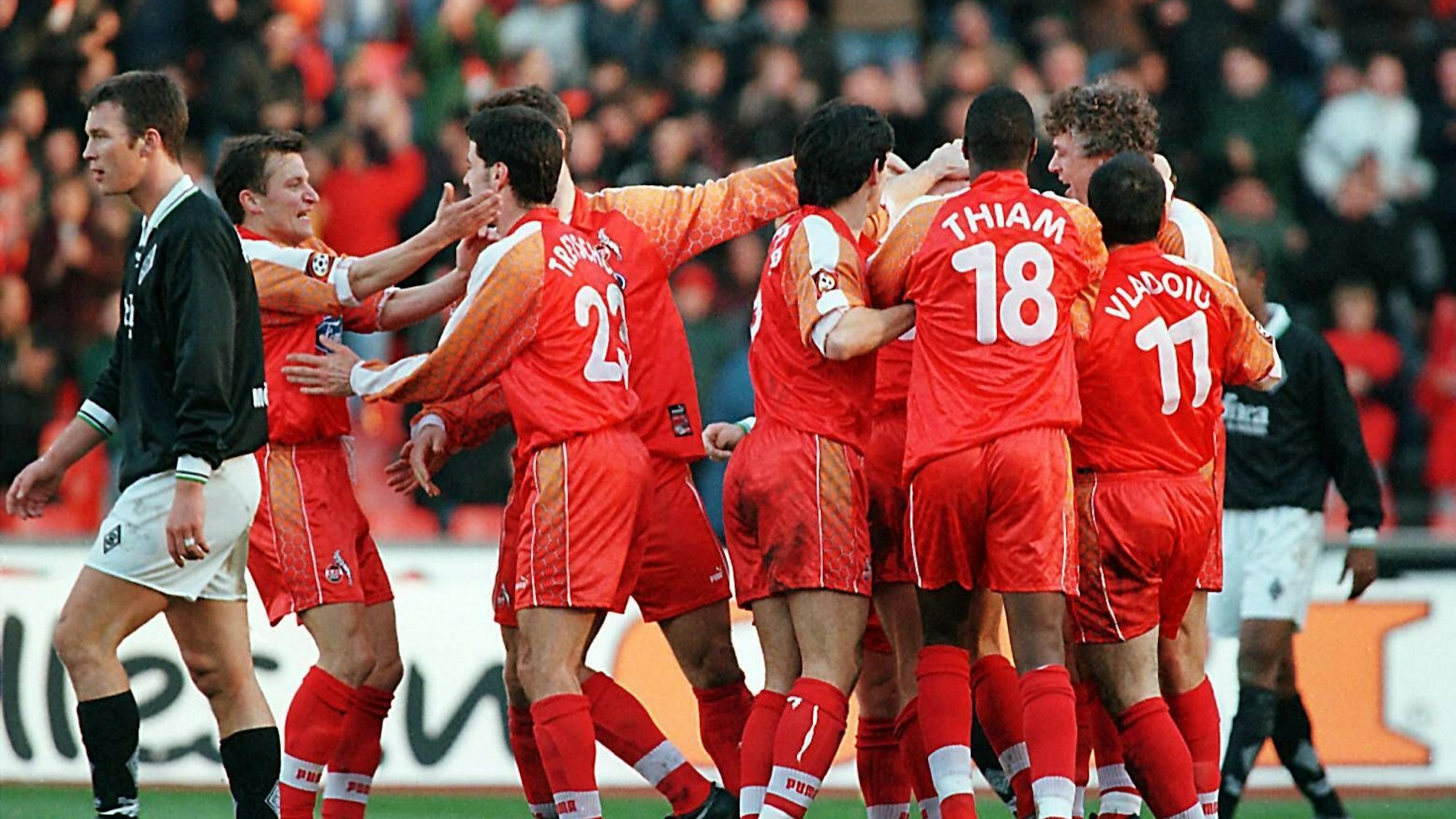 Die ganz in rot gekleideten Spieler des 1. FC Köln freuen sich in der Gruppe über ihren Sieg. Links schleicht ein Profi des Gegners enttäuscht vom Platz.
