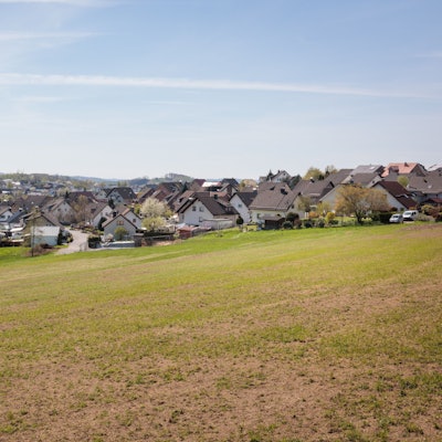 Zu sehen ist ein Wiese, im Hintergrund eine Siedlung.