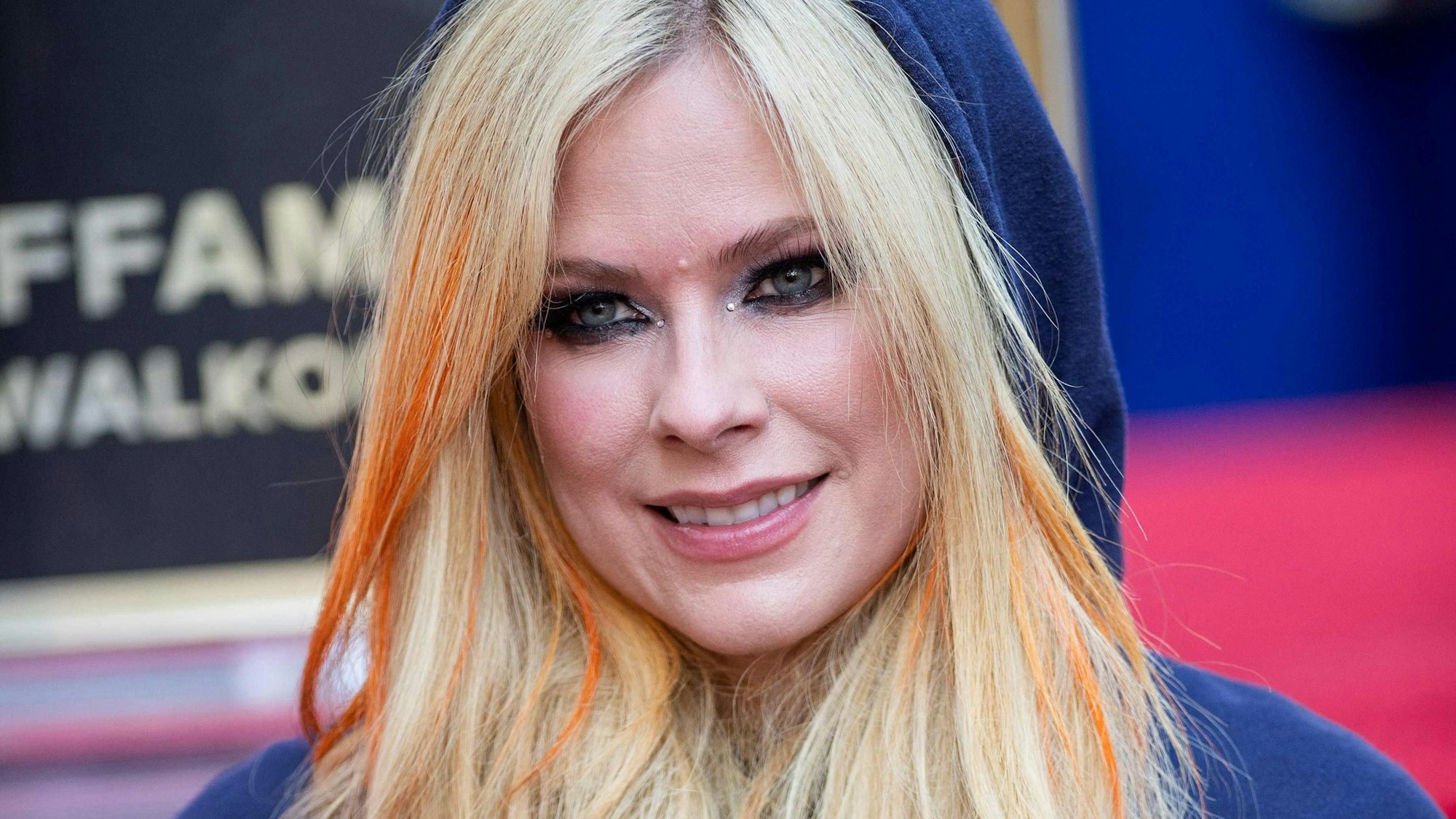 Gesicht von Avril Lavigne mit Kapuze, im Hintergrund sieht man einen roten Teppich
