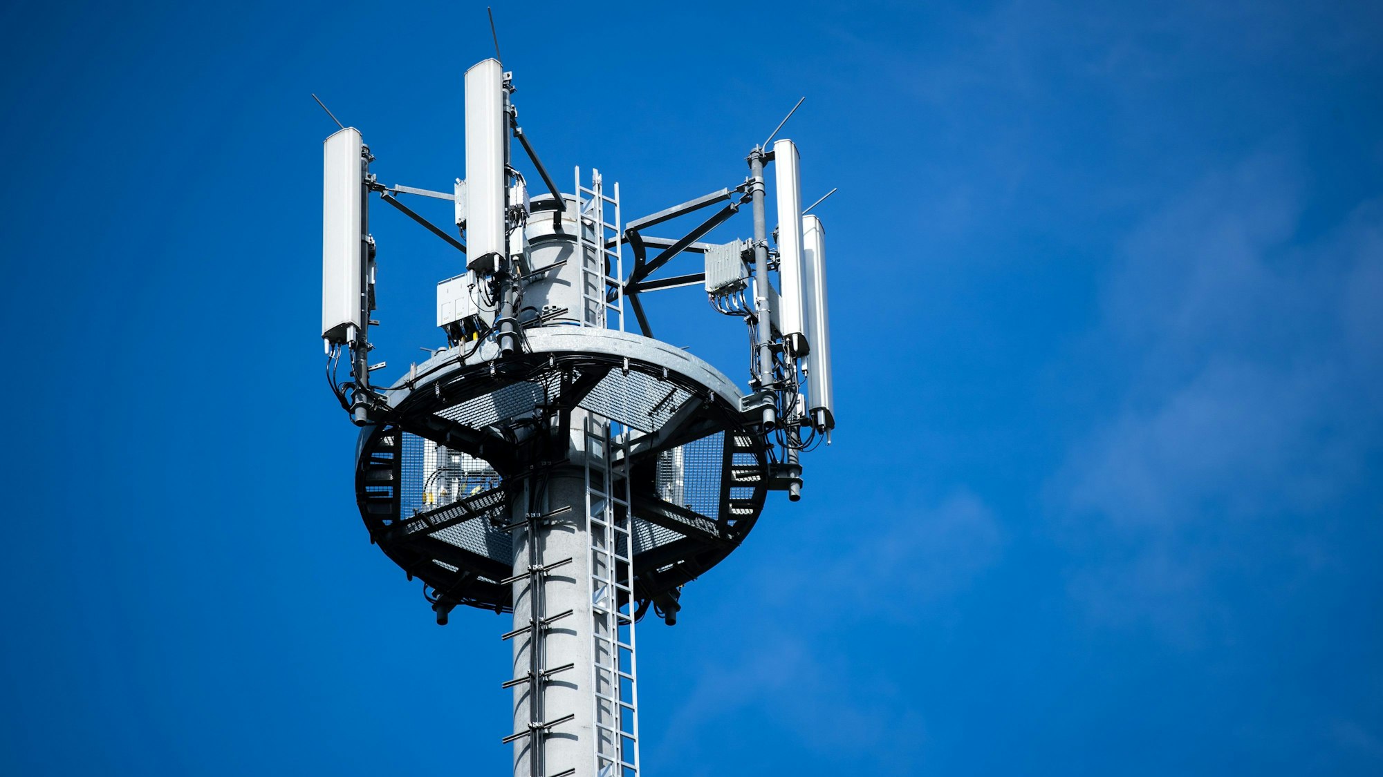 Ein Mast mit verschiedenen Antennen von Mobilfunkanbietern steht vor blauem Himmel.
Solche Antennen senden Funksignale an unsere Handys.