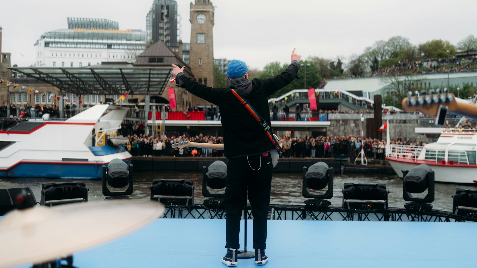 Sänger, der von einem Schiff aus aufs Ufer schaut, an dem sich Zuschauer vesammelt haben