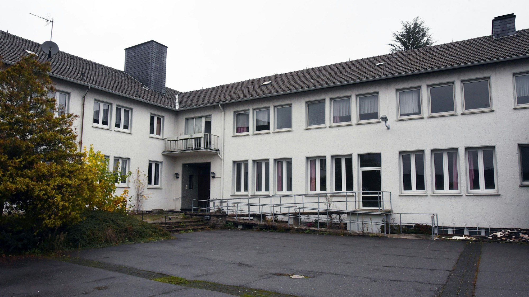 Ein weißes Gebäude mit dunklem Dach und einem asphaltierten Hof.