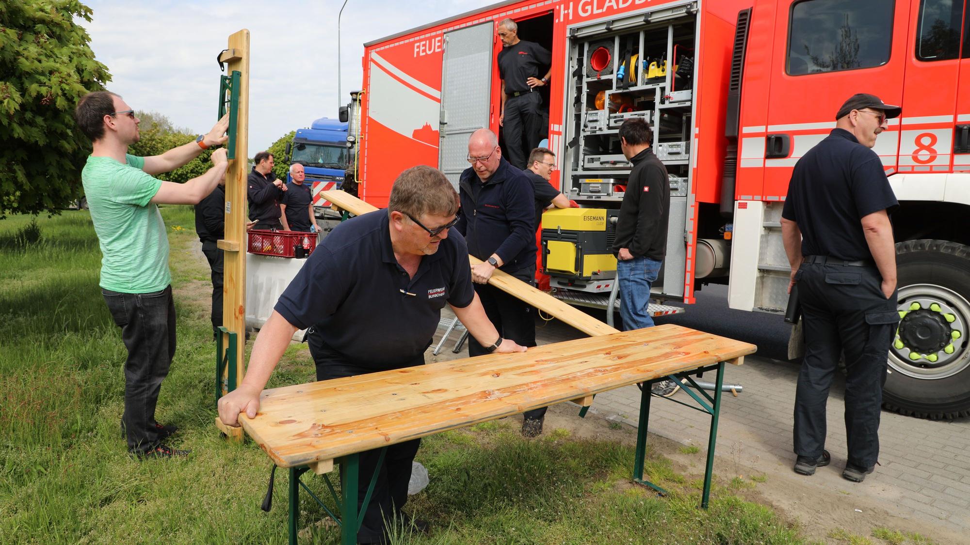 Männer klappen Tische und Bänke aus, die sie aus einem Feuerwehrfahrzeug geholt haben.
