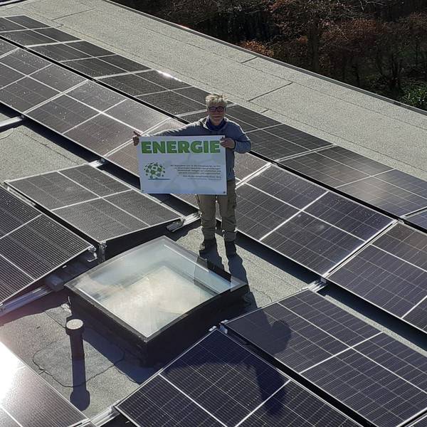 Stefan Häusler, Vorsitzender Klimafreunde Rhein-Berg, steht mit Plakat auf einem Dach mit Photovoltaikanlage.
