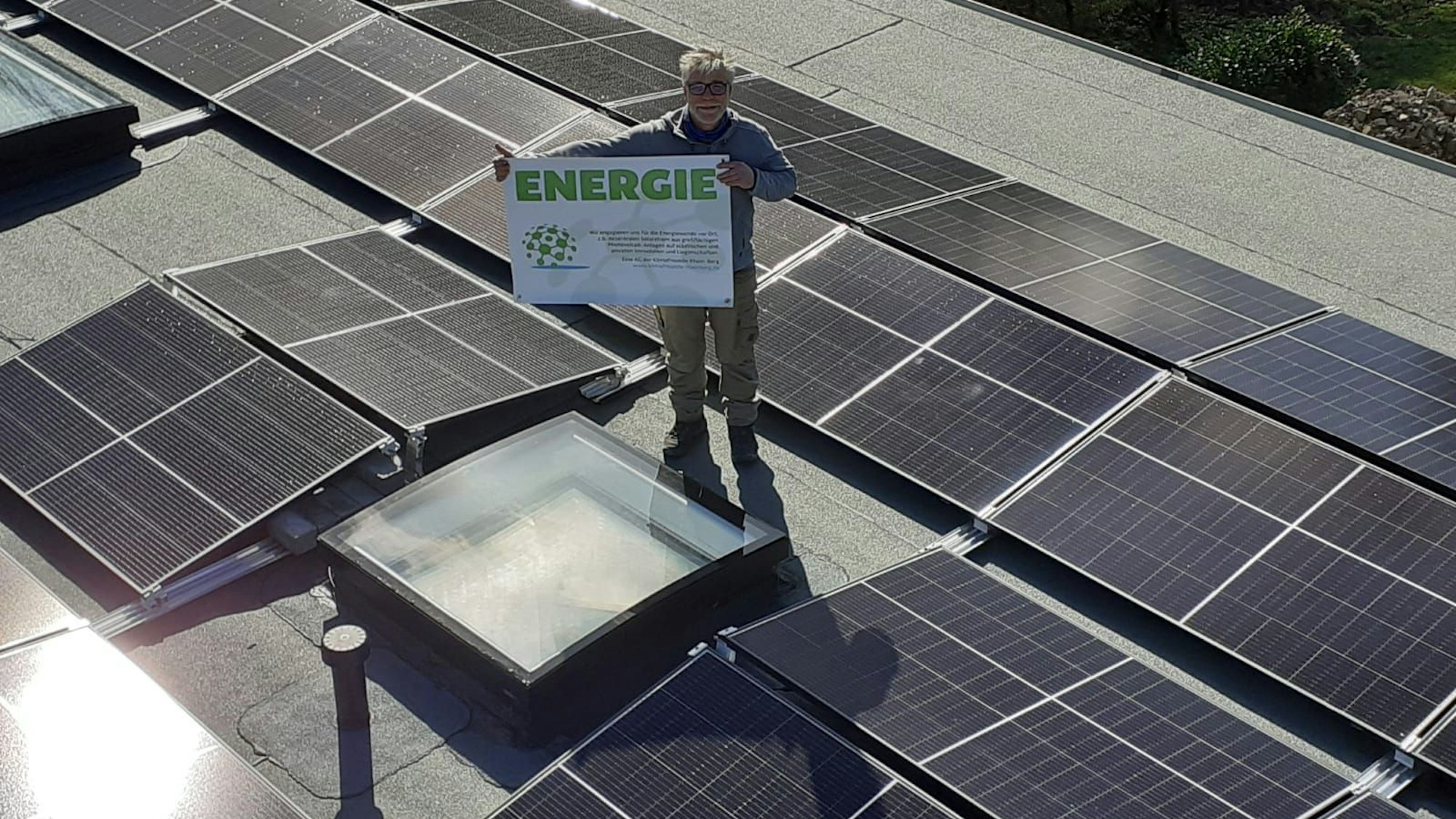 Stefan Häusler, Vorsitzender Klimafreunde Rhein-Berg, steht mit Plakat auf einem Dach mit Photovoltaikanlage.