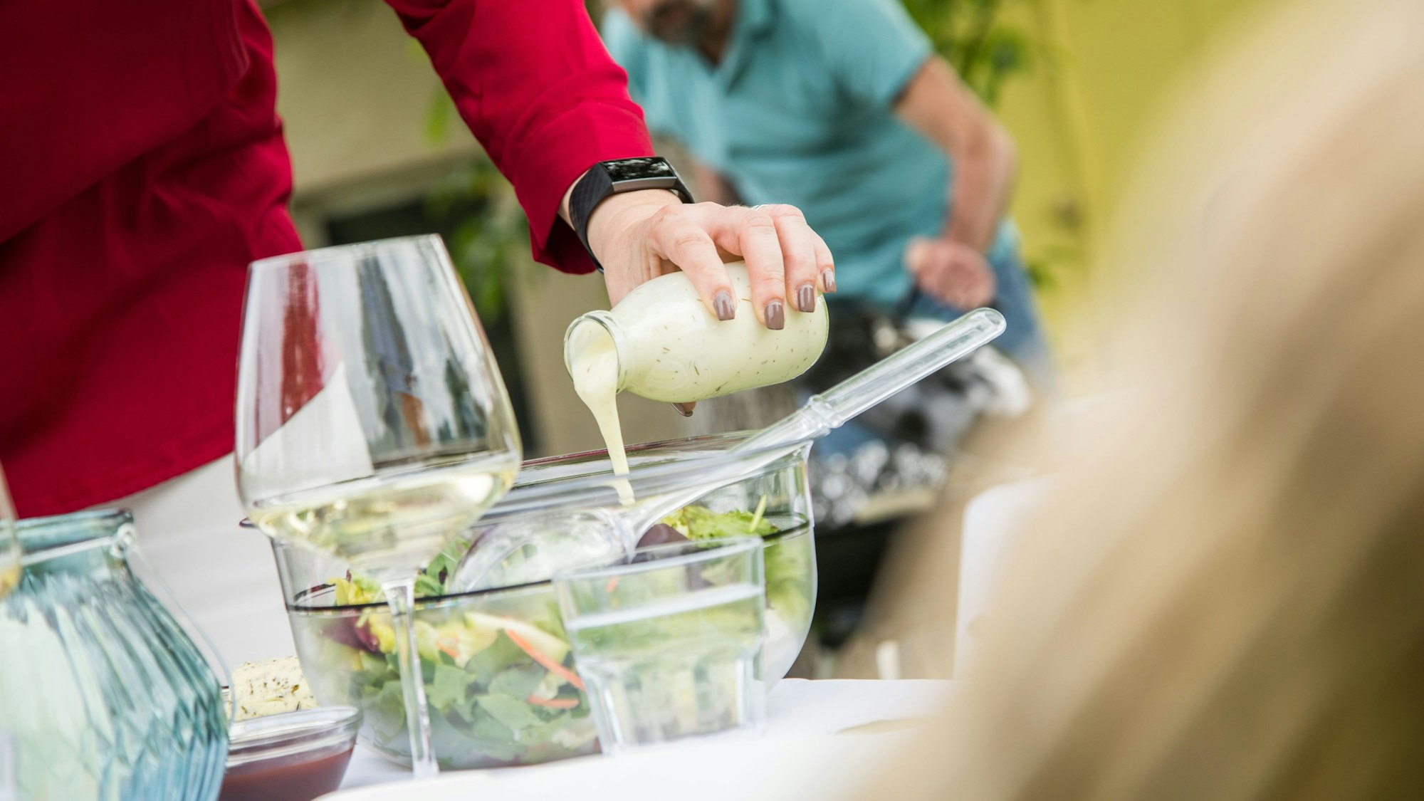 eine Frau gießt Dressing aus einer Glasflasche über einen Salat