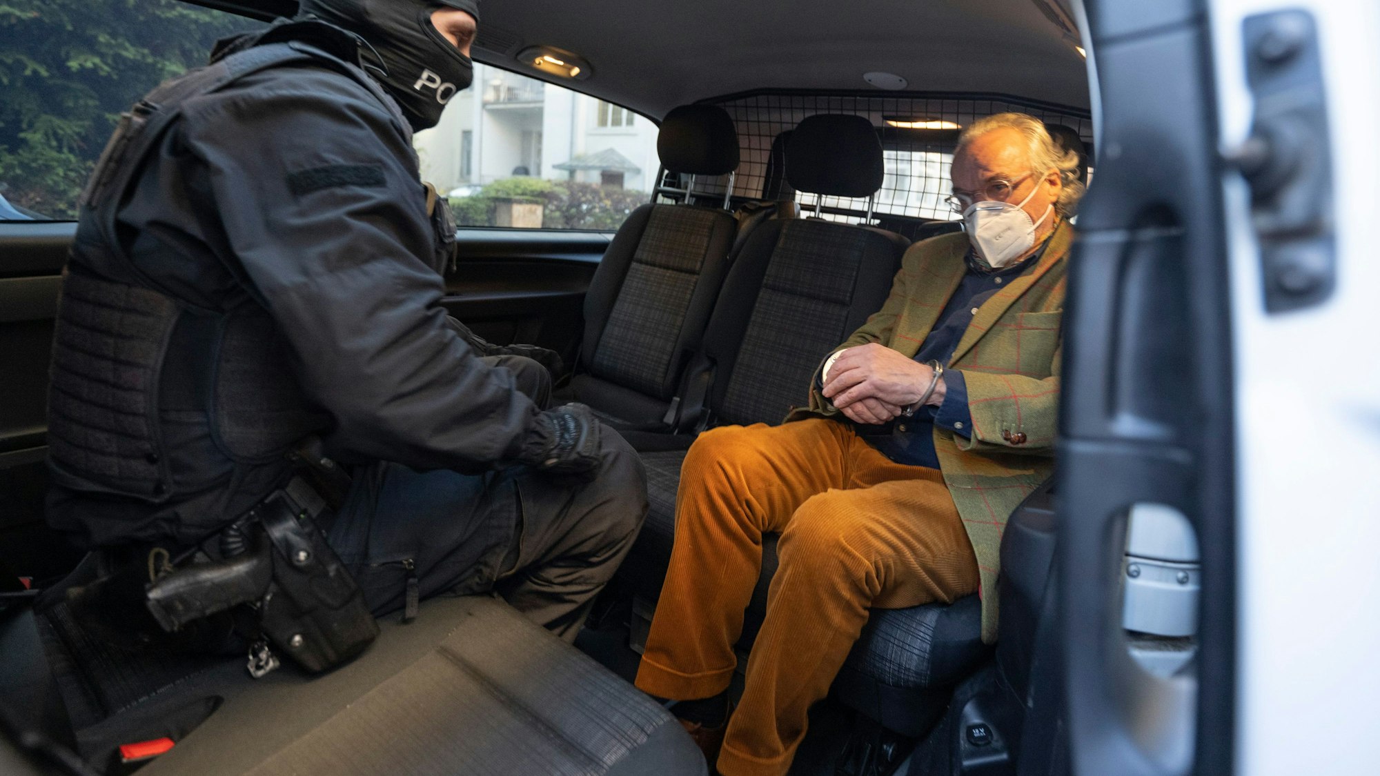 Bei einer Razzia gegen sogenannte Reichsbürger sitzt ein vermummter Polizist, nach der Durchsuchung eines Hauses, mit dem festgenommenen Heinrich XIII Prinz Reuß in einem Polizeifahrzeug. Dieser trägt dabei Handschellen.