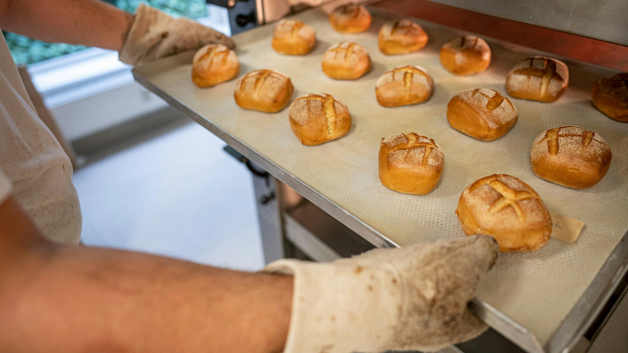 Eine Person schiebt in einer Bäckerei ein Blech mit Brötchen in den Ofen.