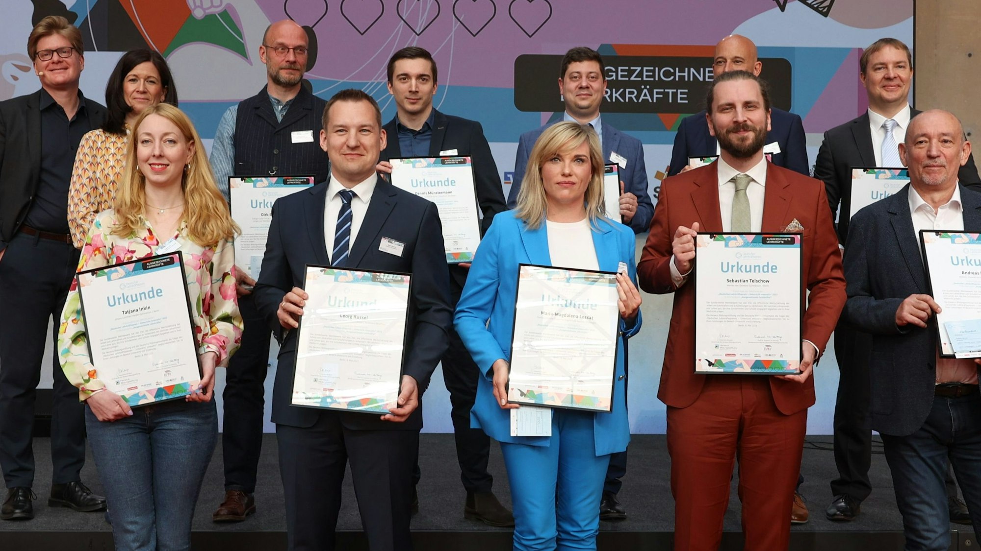 Eine Gruppe Erwachsener auf der Bühne hält Urkunden hoch.