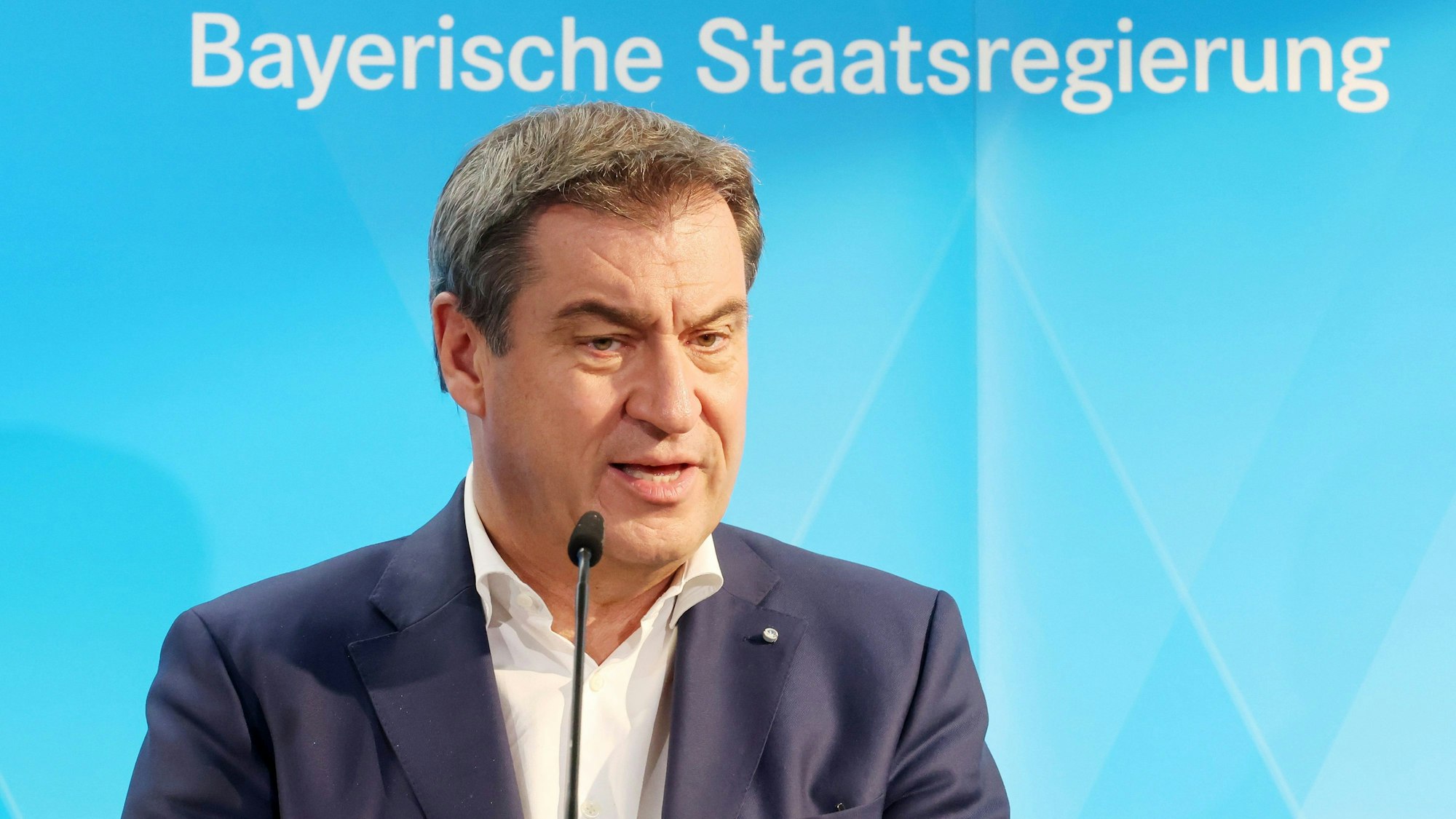 Markus Söder (CSU), Ministerpräsident von Bayern, spricht bei einer Pressekonferenz vor einem blauen Hintergrund mit der Aufschrift „Bayerische Staatsregierung“.