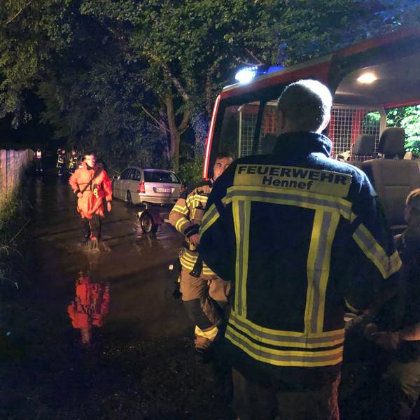 Rückblick auf die Flutnacht. Ein Feuerwehrmann der Feuerwehr Hennef schaut in Richtung eines Mannes mit orangener Jacke.