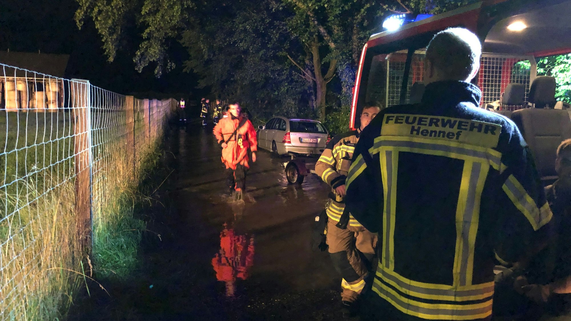 Rückblick auf die Flutnacht. Ein Feuerwehrmann der Feuerwehr Hennef schaut in Richtung eines Mannes mit orangener Jacke.